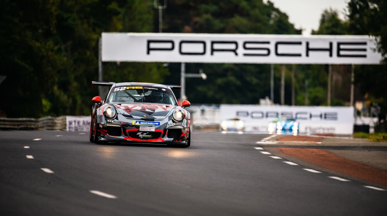 Porsche 911 GT3 Cup numéro 52, livrée camouflage gris, rouge et noir, en piste sur circuit