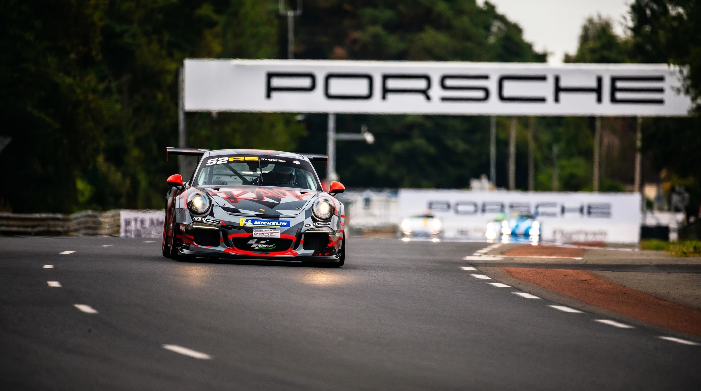 Porsche 911 GT3 Cup numéro 52, livrée camouflage gris, rouge et noir, en piste sur circuit