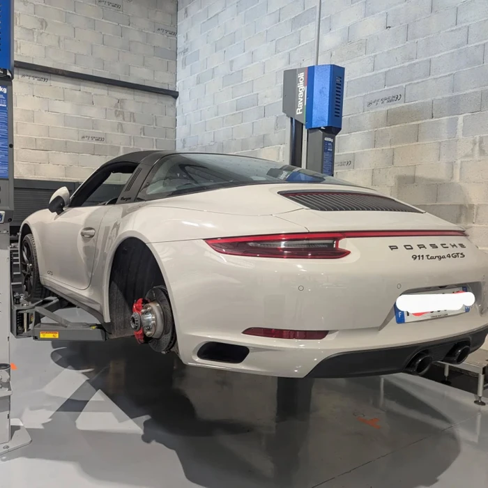 Garage automobile, deux mécaniciens en combinaisons bleues travaillent sous un véhicule surélevé