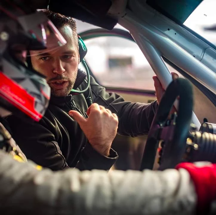 Photographe en direct d'un circuit de course automobile, montrant de l'intérieur d'une voiture de sport haute performance en action sur piste, avec vue sur le volant et la route devant, suggérant la dynamique et la concentration du pilotage de compétition. L'image doit capturer l'intensité d'une session sur circuit.