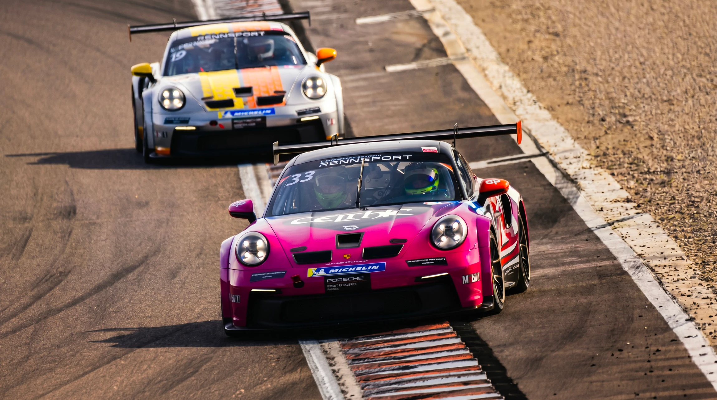 Photographie d'un pilote au volant d'une voiture de sport (type Porsche 911 ou supercar similaire) en action sur un circuit automobile, capturant un virage serré. Le pilote est concentré au volant, les mains posées correctement sur le volant, vêtu d'une tenue de pilote (combinaison de course) et d'un casque homologué. La perspective capture l'action dynamique du véhicule en mouvement avec les marquages du circuit visibles. L'image transmet l'intensité et l'expertise du pilotage sportif en environnement circuit professionnel, sans texte ni logo visible.
