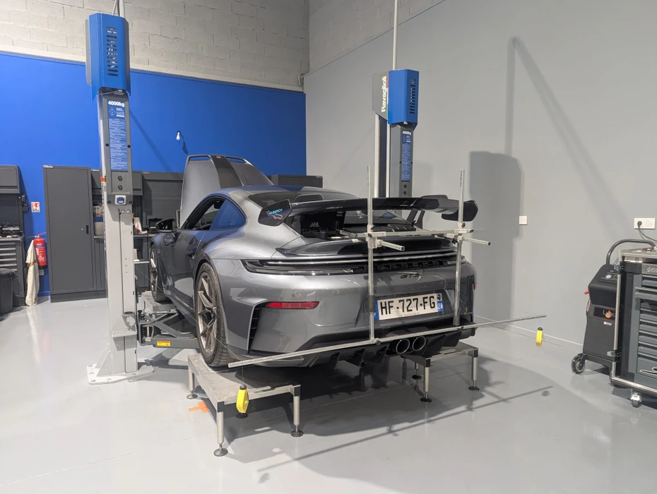 Garage automobile, deux mécaniciens en combinaisons bleues travaillent sous un véhicule surélevé
